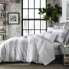 a bed with white comforter and pillows in a room next to a brick wall