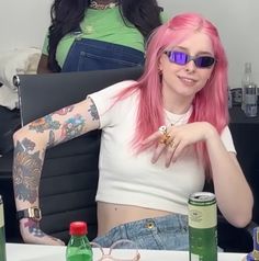 a woman with pink hair and tattoos sitting in a chair