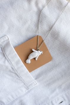 a necklace with a white dog on it is hanging from a brown piece of paper