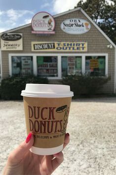 a woman holding up a cup of coffee in front of a building with signs on it