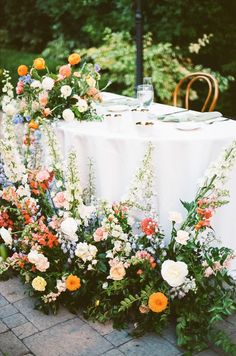 an arrangement of flowers and greenery on a table at a wedding reception in the garden