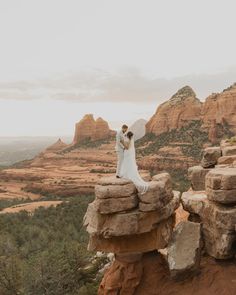 a bride and groom standing on top of a rock formation