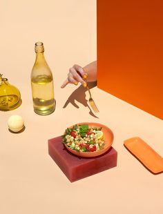 a person holding a knife and fork over a bowl of food on a table next to bottles