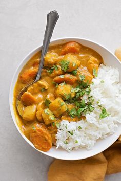 a white bowl filled with rice and chicken curry next to a wooden spoon on top of a table