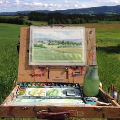 an artist's easel with paint and watercolors on it in a field