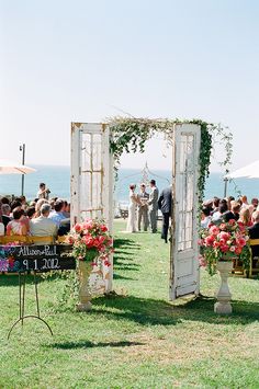 an outdoor ceremony with flowers and greenery on the grass, in front of water