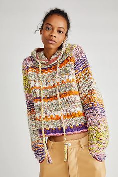 a woman wearing a multicolored sweater and tan pants with her hands in her pockets