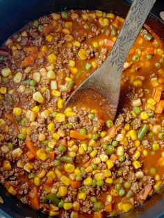 a pot filled with meat and veggies next to a wooden spoon