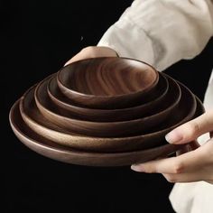 a woman holding a wooden bowl with four bowls stacked on top of each other in front of her