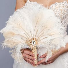 a woman in a wedding dress holding a white feathered bridal bouquet and brooch