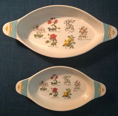 two serving trays with flowers painted on them sitting on a blue tableclothed surface