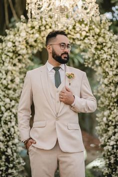 a man wearing a suit and tie standing in front of a floral arch