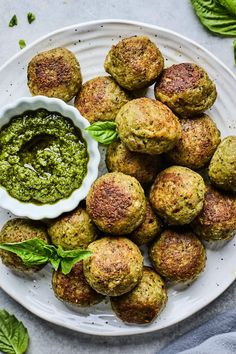 a white plate topped with meatballs covered in pesto sauce and garnished with green leaves