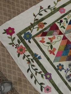 a quilted table runner with flowers and leaves on the edge, next to a pair of shoes