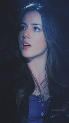 a woman with long dark hair wearing a blue shirt and black jacket looking off into the distance