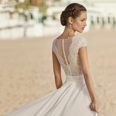 a woman standing on the beach wearing a white wedding dress with sheer neckline and open back