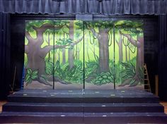 the stage is decorated with green trees and plants on black velvet curtains, along with wooden flooring