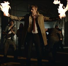 a man in a trench coat and tie holding fire torches while standing next to other men