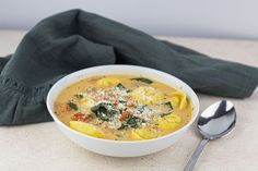 a white bowl filled with soup next to a spoon and napkin on top of a table