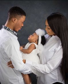 a man and woman holding a baby in their arms while standing next to each other