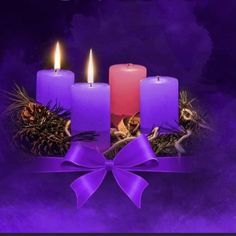 three lit candles with purple ribbon and pine cones