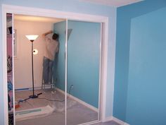 a man is painting the walls of a room with blue paint and a light on