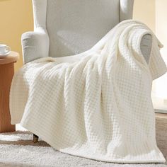 a white blanket sitting on top of a chair next to a cup and saucer