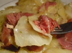 a plate with meat and potatoes on it, next to a fork that is stuck in the food