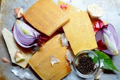 an assortment of cheeses and vegetables on a cutting board with some seasoning next to them