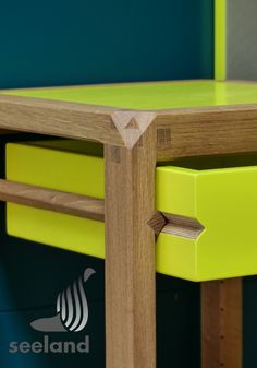 a close up of a wooden table with yellow drawers and green paint on the wall