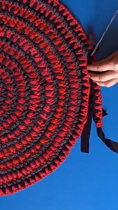 a red and black braided rug being held by someone's hand with scissors