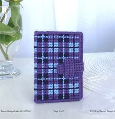 a small purple and black plaid book sitting next to a vase with a flower in it