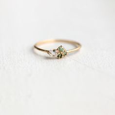 a gold ring with two green and white stones on it, sitting on a white surface