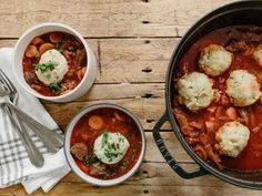 two bowls filled with stew and dumplings on top of a wooden table next to silverware