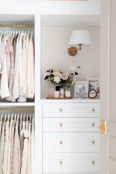 an open closet with clothes hanging on the wall and flowers in vase next to it