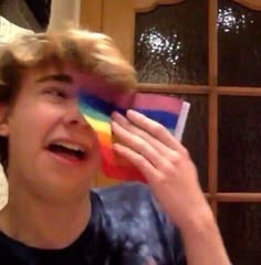 a young boy is laughing and holding a rainbow flag in front of his face with the caption kak xe sto ayeho