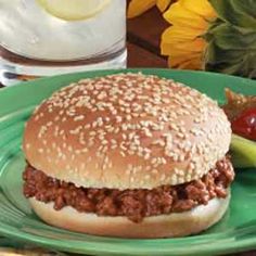 a sloppy joe sandwich on a green plate with pickles and ketchup next to it