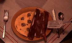 a plate with bacon and cheese on it next to utensils, forks and spoons