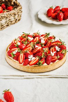 a strawberry tart on a table with strawberries and other fruit in the background