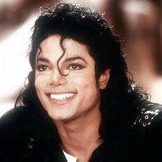 michael jackson smiling for the camera with his hair in curls and wearing a black jacket