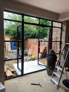 a man sitting on a step ladder in front of a glass door that is being built