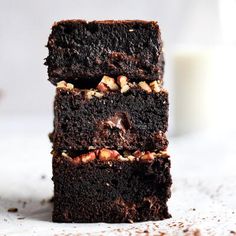 three chocolate brownies stacked on top of each other with nuts and milk in the background