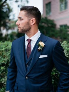 a man wearing a suit and tie standing in front of bushes