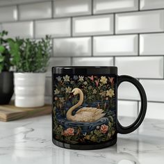 a black coffee mug with a white swan on the water surrounded by flowers and plants