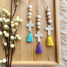 three necklaces with tassels and beads on a wooden tray next to a plant