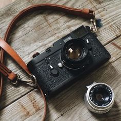 an old fashioned camera sitting on top of a wooden table next to a leather strap