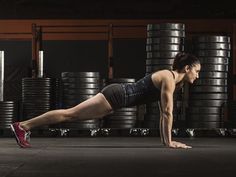 a woman doing push ups in a gym with lots of tires behind her and one leg on the ground