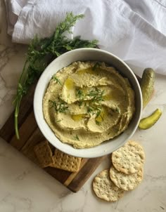 a white bowl filled with hummus and crackers on top of a cutting board