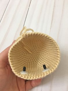 a hand holding a woven basket with two black buttons on the front and one white button on the back