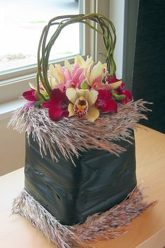 a square cake with flowers and grass on the top is sitting on a table near a window